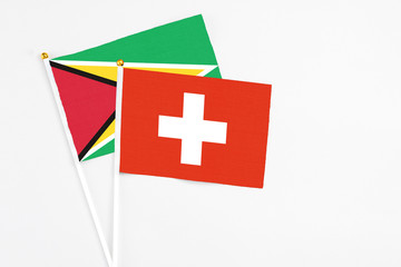 Obraz premium Switzerland and Guyana stick flags on white background. High quality fabric, miniature national flag. Peaceful global concept.White floor for copy space.