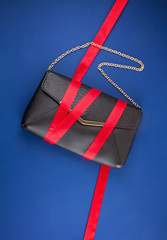Black hand bag with red ribbon over the dark blue background.
