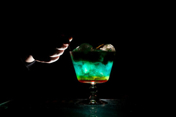 bartender makes a multi-colored cocktail with ice and foam in a glass on a black background, hands hold the drink