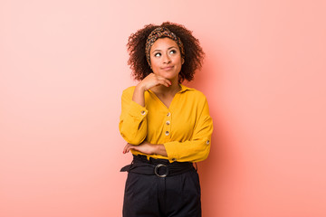 Young african american woman against a pink background looking sideways with doubtful and skeptical...