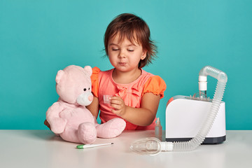 Cute little girl playing with nebulizer and teddy bear. Studio shoot. Allergy concept