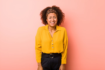 Obraz na płótnie Canvas Young african american woman against a pink background laughs and closes eyes, feels relaxed and happy.