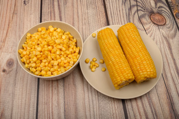 Two ears of boiled corn in a plate and a grain of corn on the table. Healthy diet. Fitness diet. For a sweet treat.
