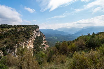 Fototapeta na wymiar Rocky hill with green trees and blue mountains on the background, Tavertet, Barcelona province, Catalonia.