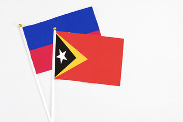 East Timor and Haiti stick flags on white background. High quality fabric, miniature national flag. Peaceful global concept.White floor for copy space.