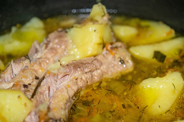 Stewed pork ribs with potatoes, onions, carrots and dill in a saucepan. Close up. Traditional recipe. Home cooking.