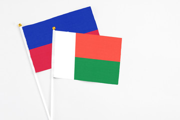 Madagascar and Haiti stick flags on white background. High quality fabric, miniature national flag. Peaceful global concept.White floor for copy space.