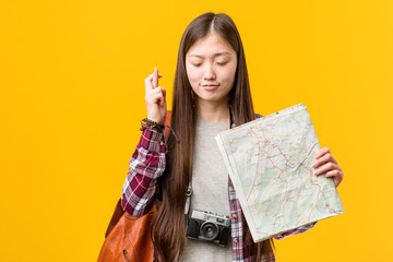 Young asian woman holding a map crossing fingers for having luck