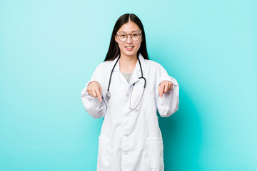 Young chinese doctor woman points down with fingers, positive feeling.