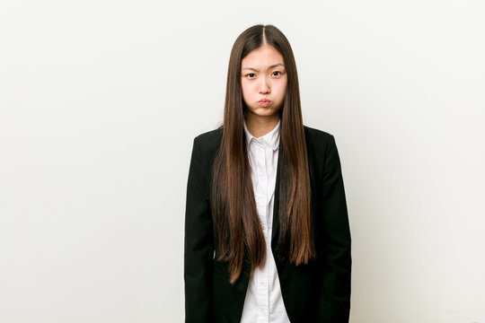 Young pretty chinese business woman blows cheeks, has tired expression. Facial expression concept.