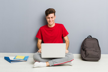 Young student man sitting on his house floor holding a laptop