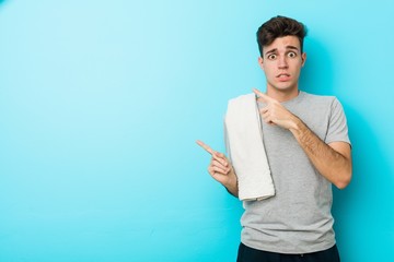 Young fitness teenager man shocked pointing with index fingers to a copy space.