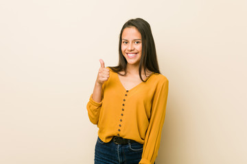 Young hispanic woman against a beige background smiling and raising thumb up
