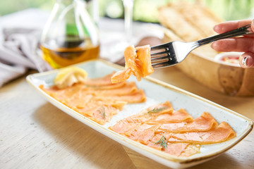 Closeup of salted and smoked salmon or trout fillet on a fork . Thin slices of red fish with lemon close up. Restaurant menu