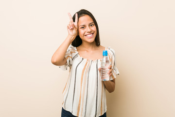 Young hispanic woman holding a bottle of water showing victory sign and smiling broadly.