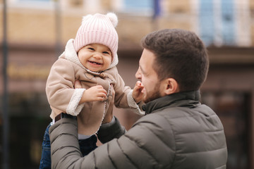 Fototapeta premium Adorable little girl on father's hands. Cute baby girl laughing. Father with daughter in the city