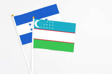 Uzbekistan and Honduras stick flags on white background. High quality fabric, miniature national flag. Peaceful global concept.White floor for copy space.