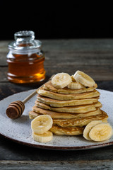 pancakes lie on a plate poured with honey with a honey spoon and decorated with bananas. plate with pancakes on an old wooden background  with place for inscription