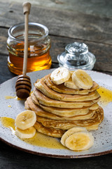 pancakes lie on a plate poured with honey with a honey spoon and decorated with bananas. plate with pancakes on an old wooden background.