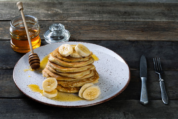 pancakes lie on a plate poured with honey with a honey spoon and decorated with bananas. plate with pancakes on an old wooden background.