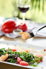 Close-up of grilled shrimps on a fork. Woman eats Delicious salad with slice grapefruit and arugula salad and spicy fried prawns. Restaurant menu, natural and organic food concept.