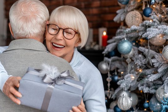 Senior couple hugging with gifts in front of Christmas tree at home living room