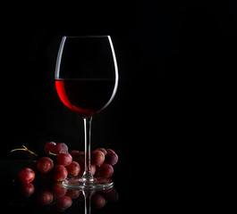 Glass of red wine and bunch of grapes on the dark background