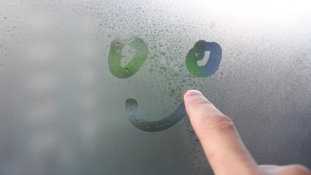 A finger paints a smile on a foggy window. Joyful sign on glass in rainy weather