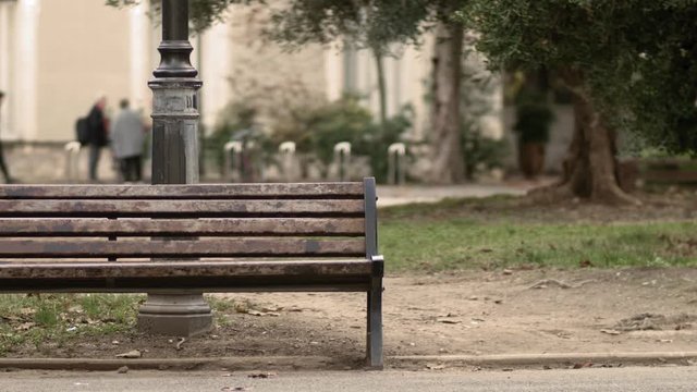 Old wooden bench in a park during a cold weather with people talking in the background. 
