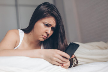 Sad news. Upset young woman with mobile phone reads the message