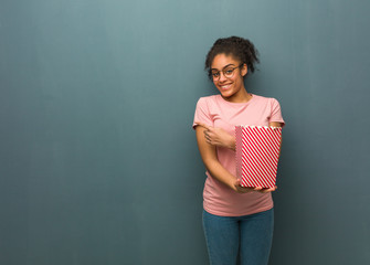 Young black woman smiling and pointing to the side. She is holding a popcorns bucket.