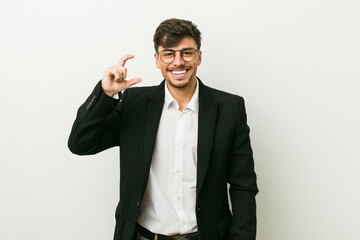 Young business hispanic man holding something little with forefingers, smiling and confident.