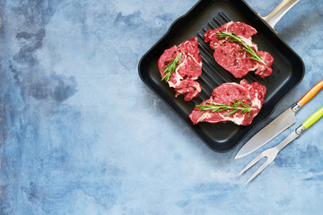 Three Fresh raw beef steaks with rosemary and pepper in pan on blue background. Top view, copy space