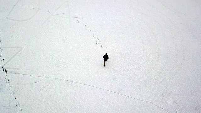 Aerial tracking shot of Young man walking on a frozen lake bed with some letters etched in the ice, Jasper National Park, Alberta Canada