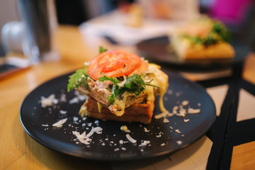 Waffles sandwich with bacon chiken and frech salad on black plate. Background of wooden table