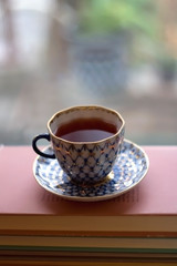 Tea in a vintage porcelain cup on stack of pastel colored books. Selective focus.