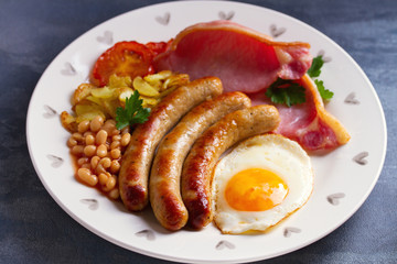 Sausages, bacon, egg, tomatoes, fries and beans on white plate. horizontal image