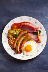 Sausages, bacon, egg, tomatoes, fries and beans on white plate. Overhead vertical image