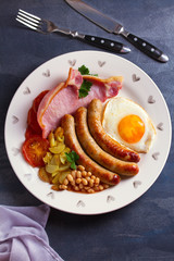 Sausages, bacon, egg, tomatoes, fries and beans on white plate. Overhead vertical image