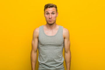 Young caucasian sport man shrugs shoulders and open eyes confused.