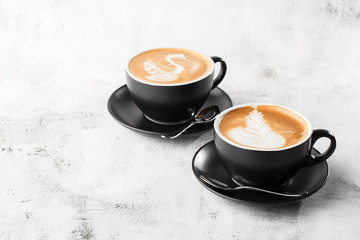 Two black cups of hot latte coffee with beautiful milk foam latte art texture isolated on bright marble background. copy space. Advertising for cafe menu. Coffee shop menu. Horizontal photo.