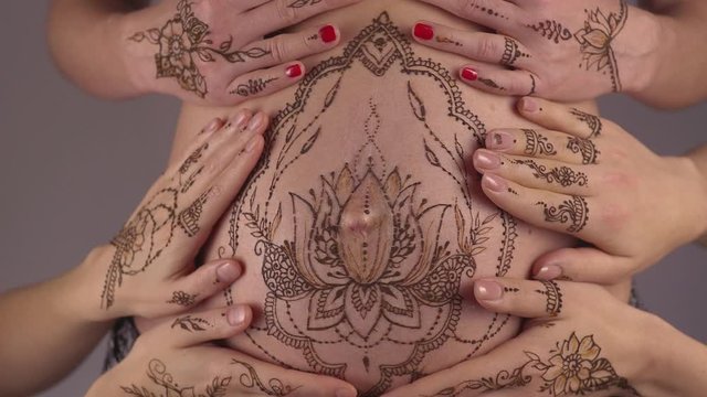 Close up of pregnant belly with mehendi henna tattoo surrounded by loving female hands. Motherhood concept, happy maternity