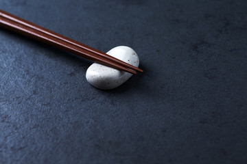 Wooden chopsticks and chopstick rest on dark stone background. Close up. Copy space. 