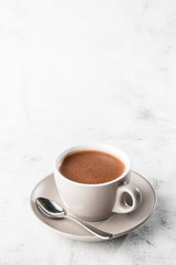 Cup of hot cocoa or hot chocolate or americano in white cup isolated on bright marble background. Overhead view, copy space. Vertical photo. traditional drinks for winter time