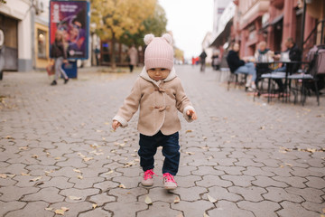 Adorable little baby girl in beautiful brown coat walking in the city. Cute eleven month baby smile and run