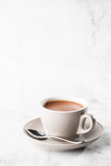 Cup of hot cocoa or hot chocolate or americano in white cup isolated on bright marble background. Overhead view, copy space. Vertical photo. traditional drinks for winter time
