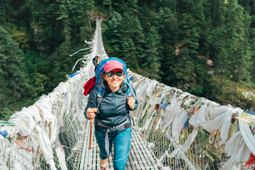 Young smiling female photographer crossing canyon over Suspension Bridge decorated with...