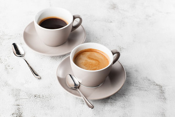 Two white cups of hot black coffee with milk isolated on bright marble background. Overhead view, copy space. Advertising for cafe menu. Coffee shop menu. Horizontal photo.