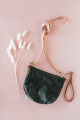 Modern green leather bag on pink background with dried flower