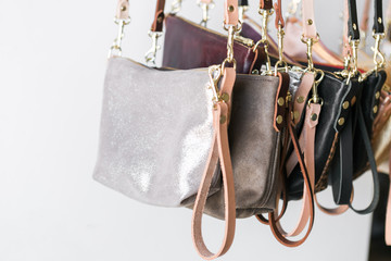 Bunch of small leather purses hanging from rack, white background, close up